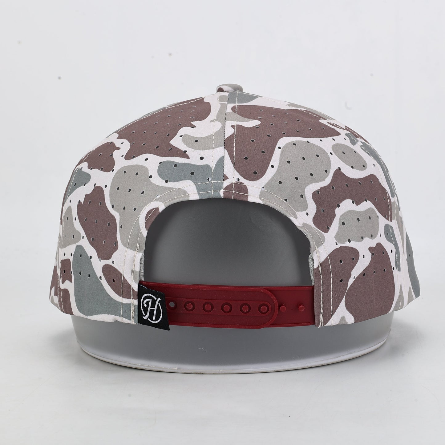 Camouflage-patterned cap with a red band and logo on a light gray background