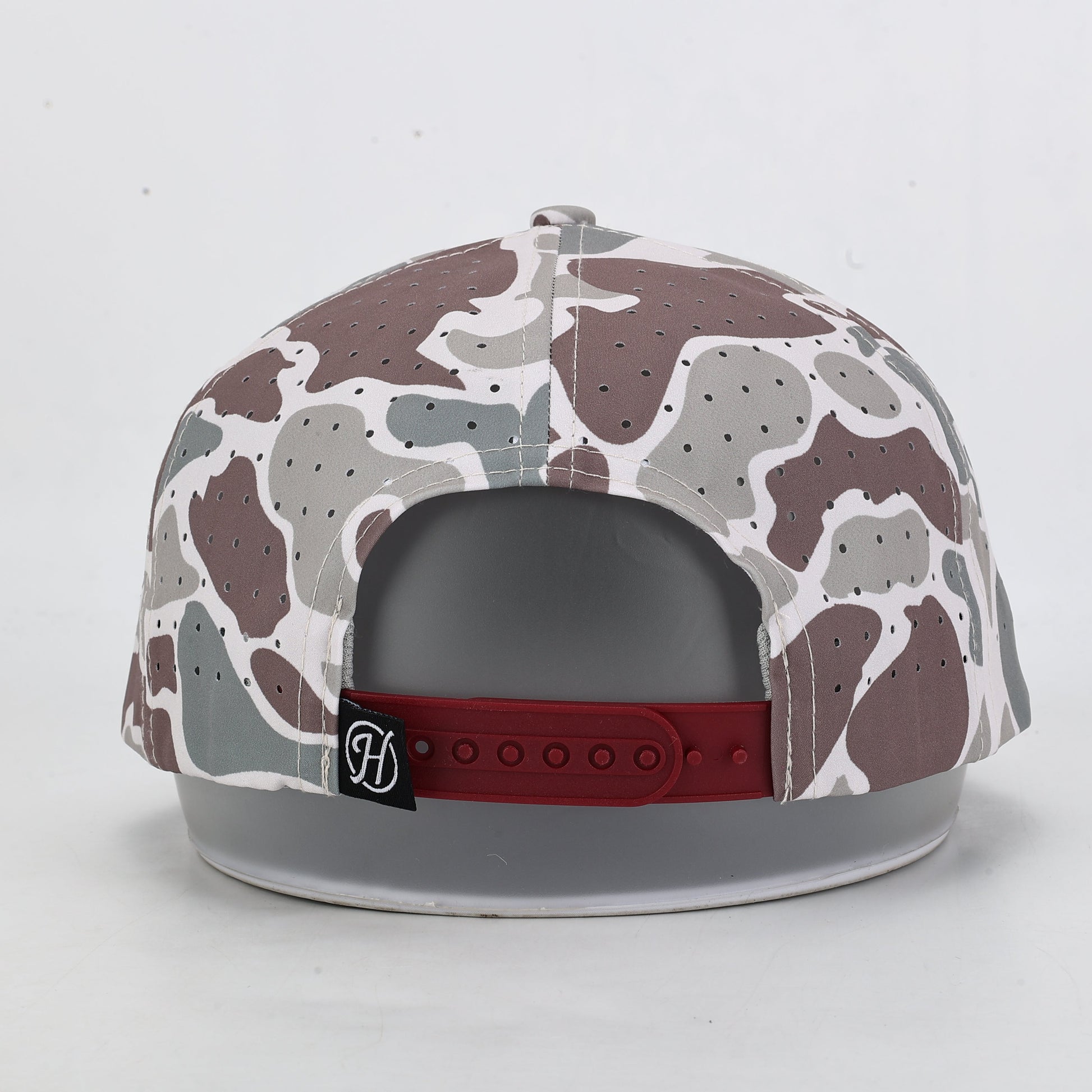 Camouflage-patterned cap with a red band and logo on a light gray background